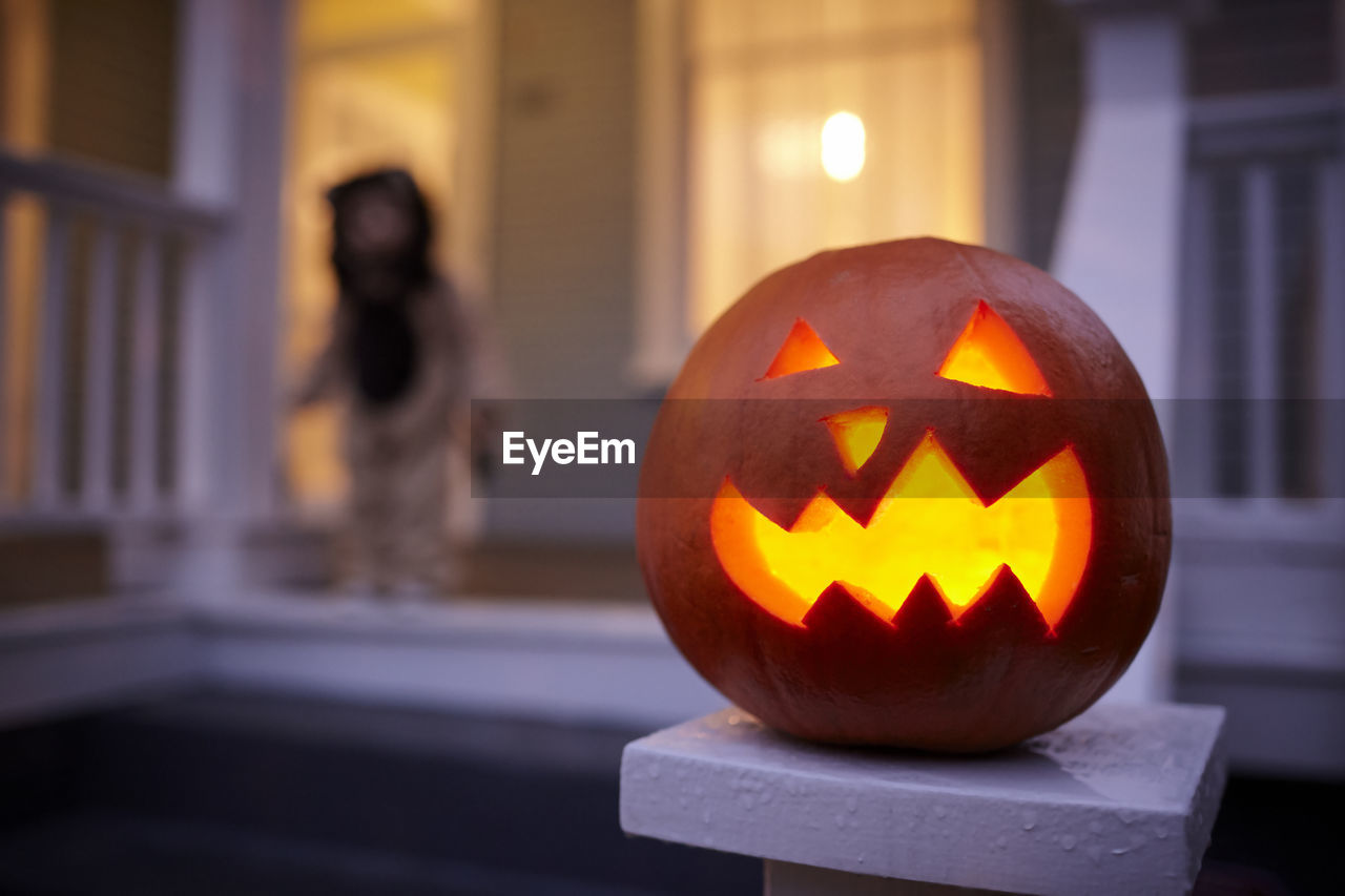 Close-up of jack o lantern with baby boy in background at dusk