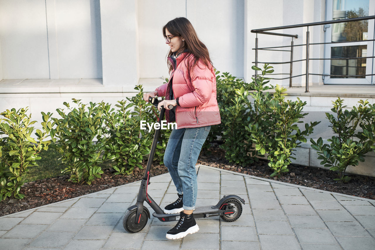 Millennial young girl in a pink jacket on an electric scooter