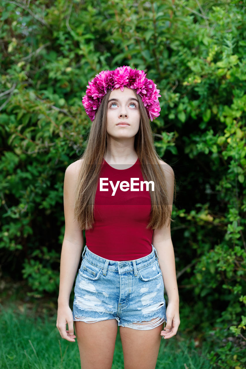 PORTRAIT OF BEAUTIFUL YOUNG WOMAN STANDING AGAINST PINK PLANTS