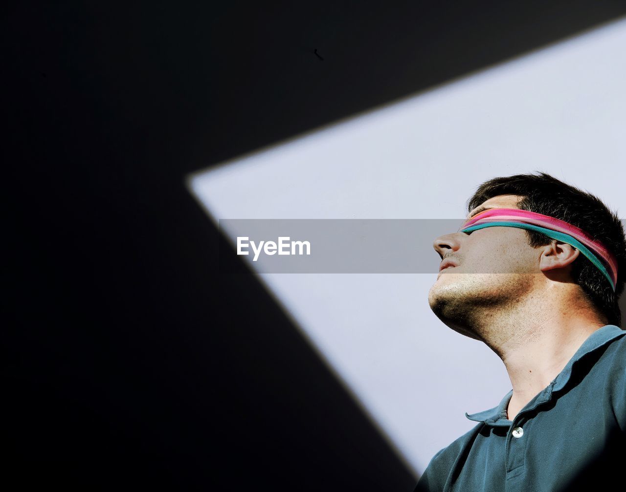 Low angle view of man with fabric on eyes against wall