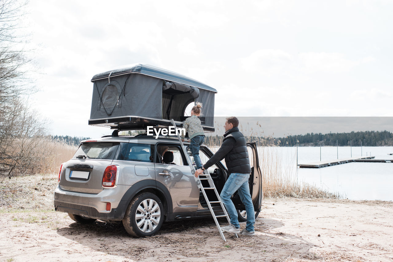 Father helping his daughter climb a ladder to a roof top tent camping