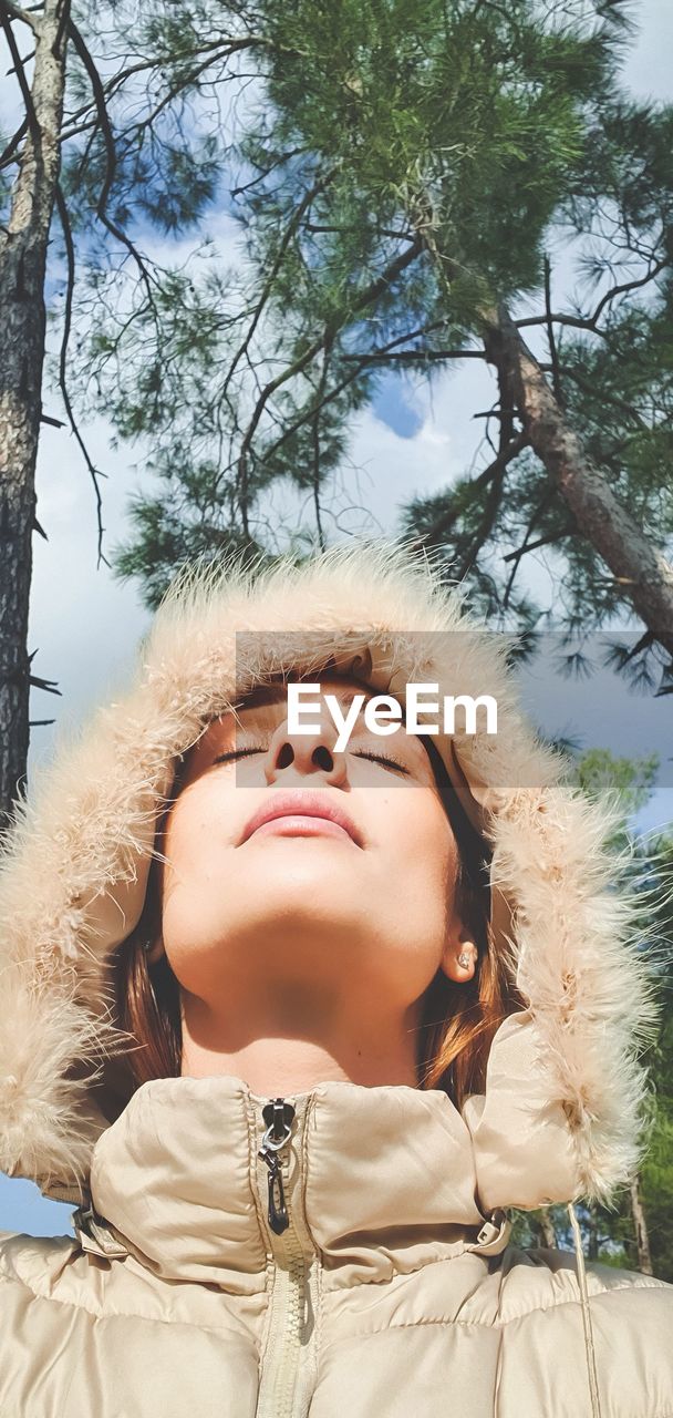 Low angle view of woman wearing fur hat with closed eyes against tree