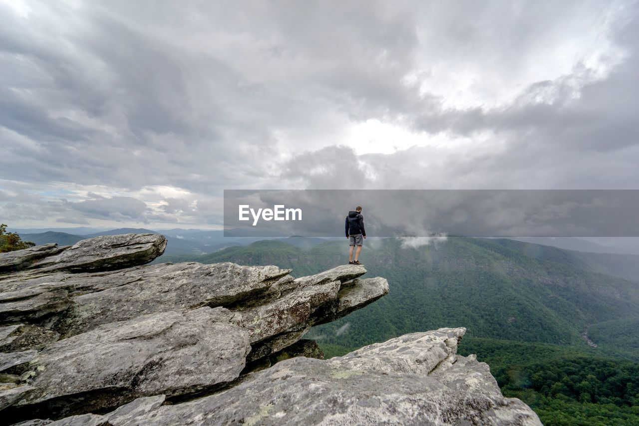 Rear view of male hiker standing on mountain against cloudy sky