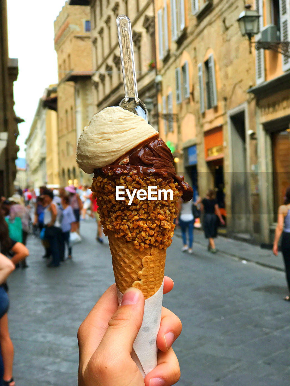 CROPPED HAND HOLDING ICE CREAM CONE AGAINST CITY
