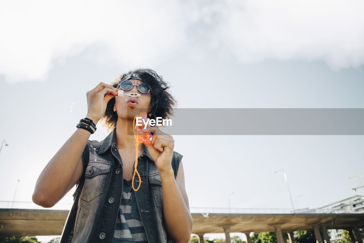 Low angle view of young man blowing soap bubbles against sky