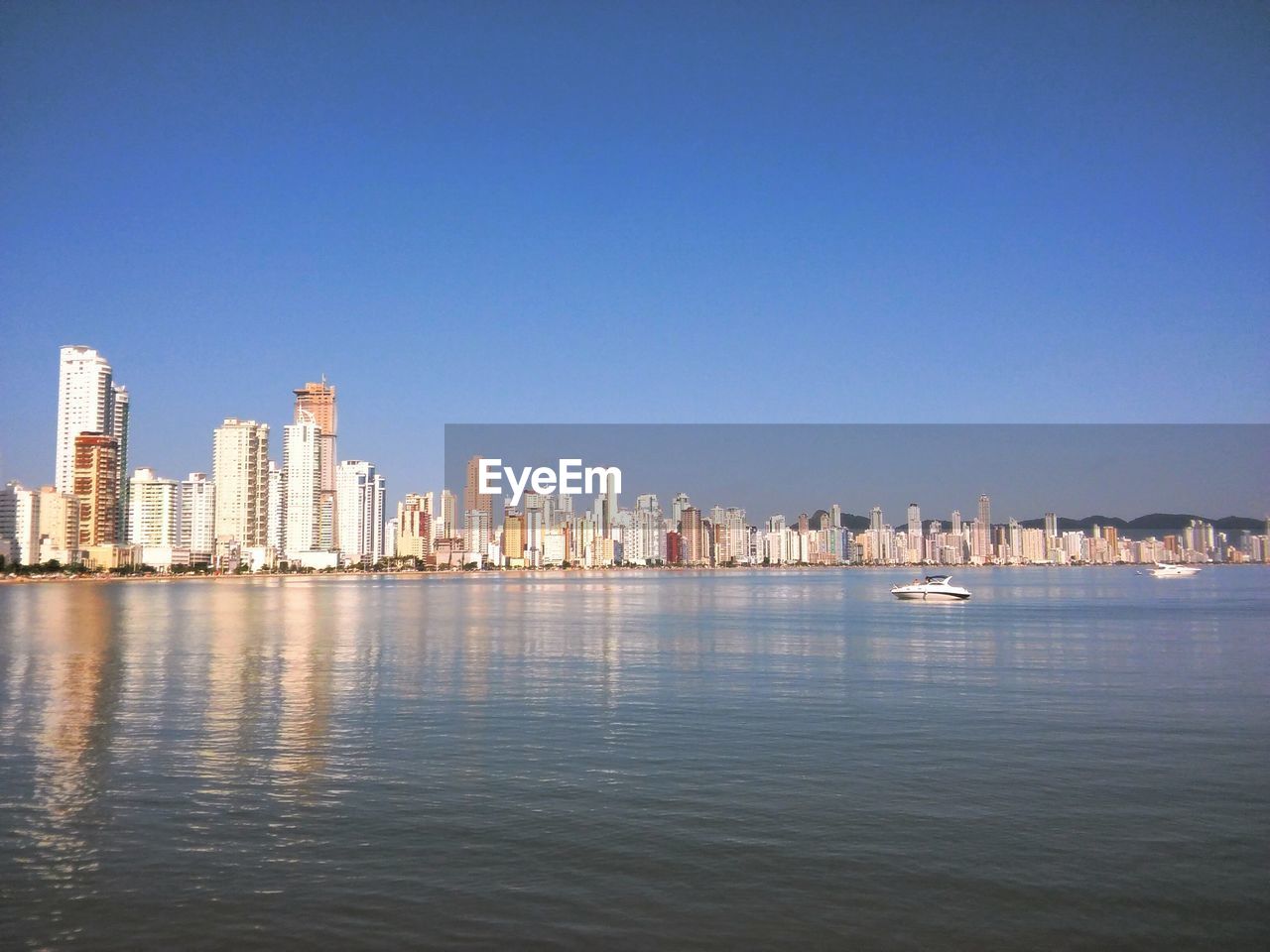 Sea by cityscape against clear blue sky