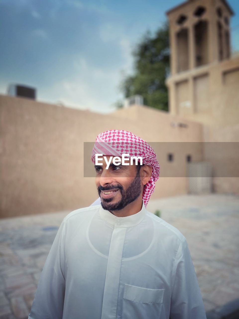 Smiling man in traditional clothing looking away while standing against built structure