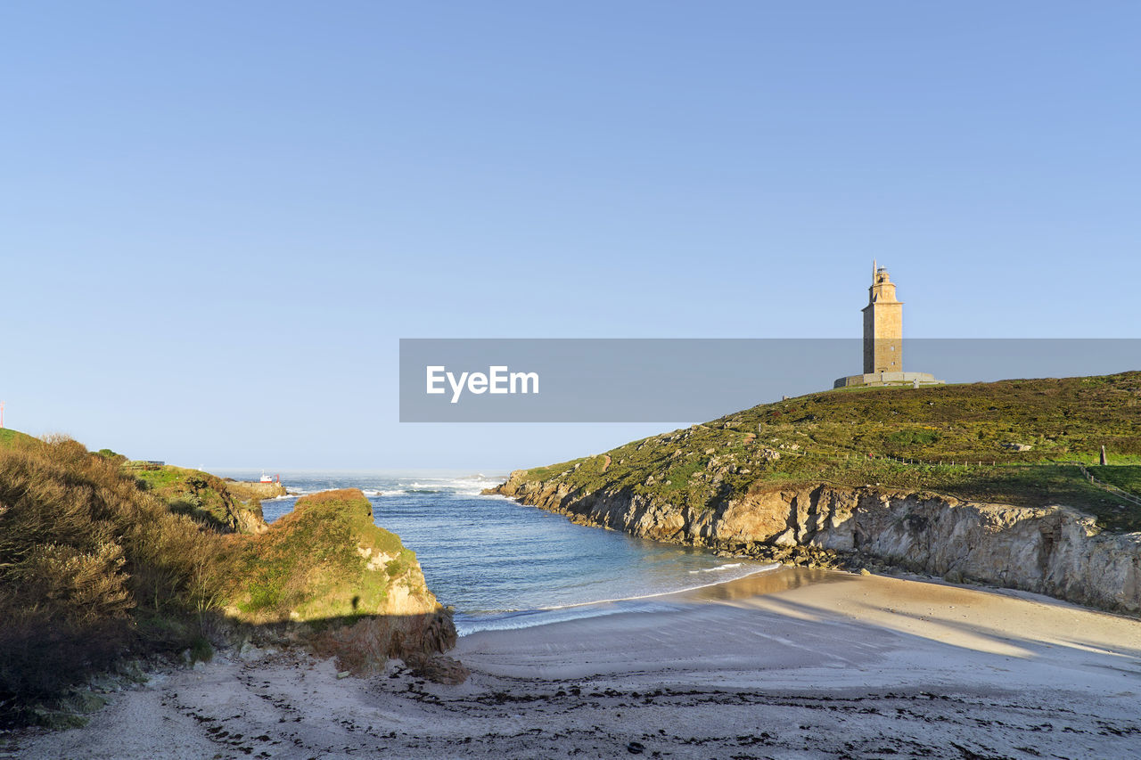 Lighthouse by sea against clear sky