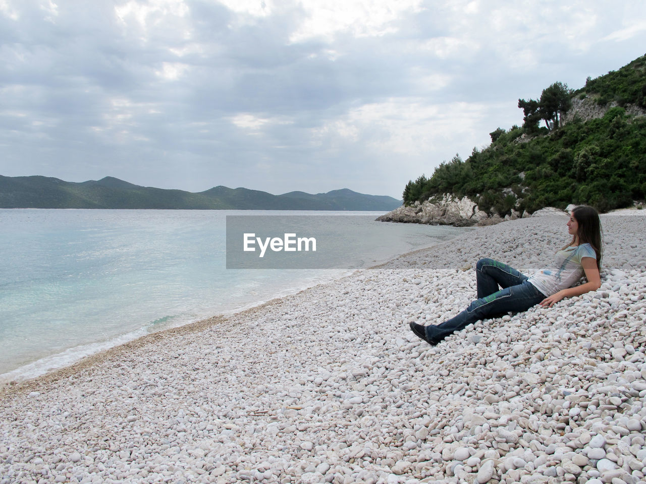 Side view of woman relaxing on beach against sky