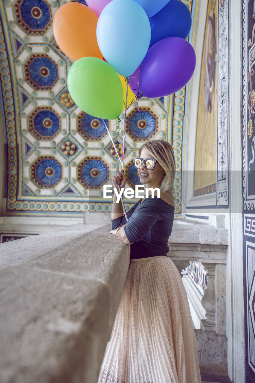 Portrait of happy young woman holding balloons at historic place