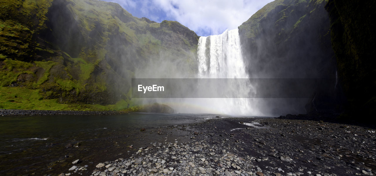 SCENIC VIEW OF WATERFALL BY ROCKS AGAINST MOUNTAIN