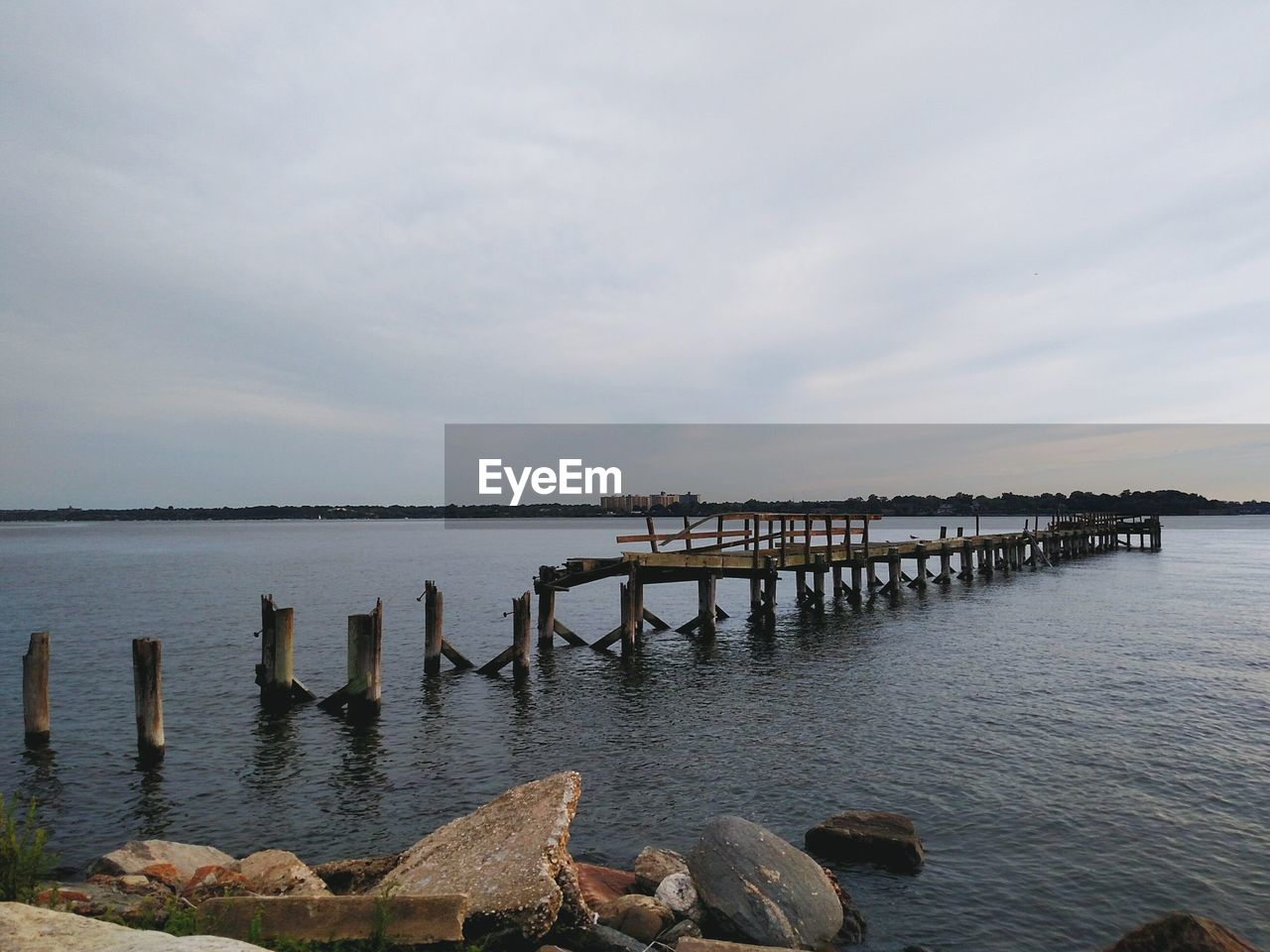 Damaged pier amidst sea against cloudy sky