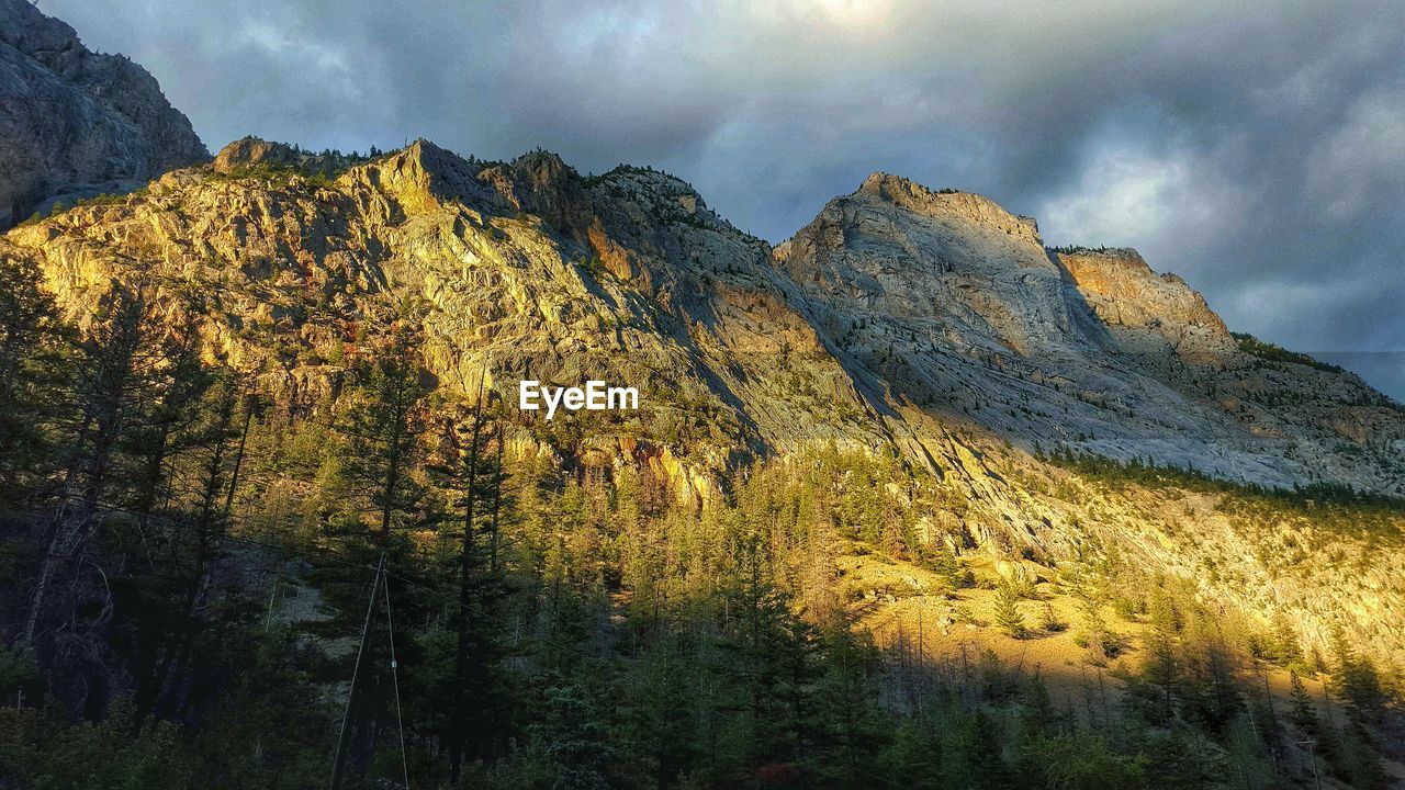 Low angle view of rocky mountains against cloudy sky