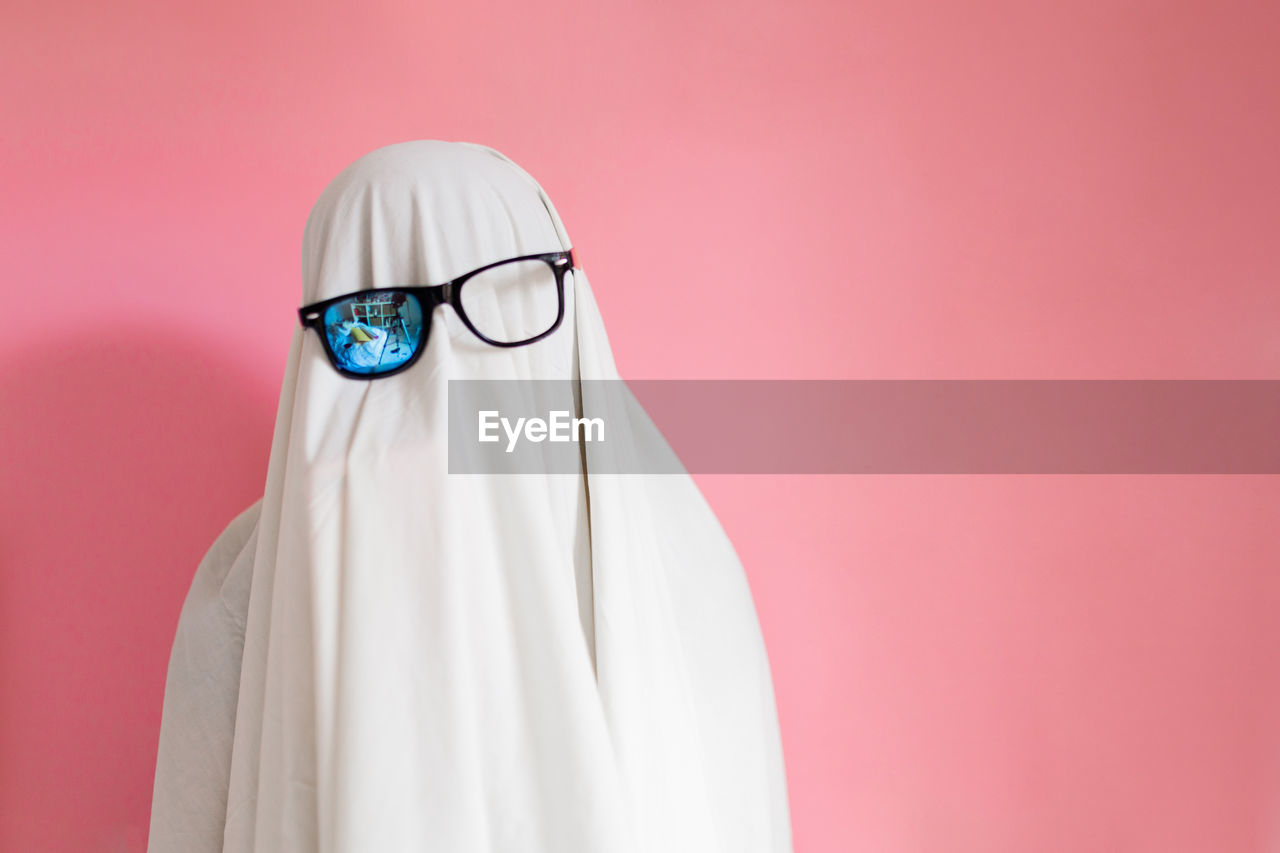 Cute sheet ghost costume with sunglasses on a pink background. halloween party carnival concept.