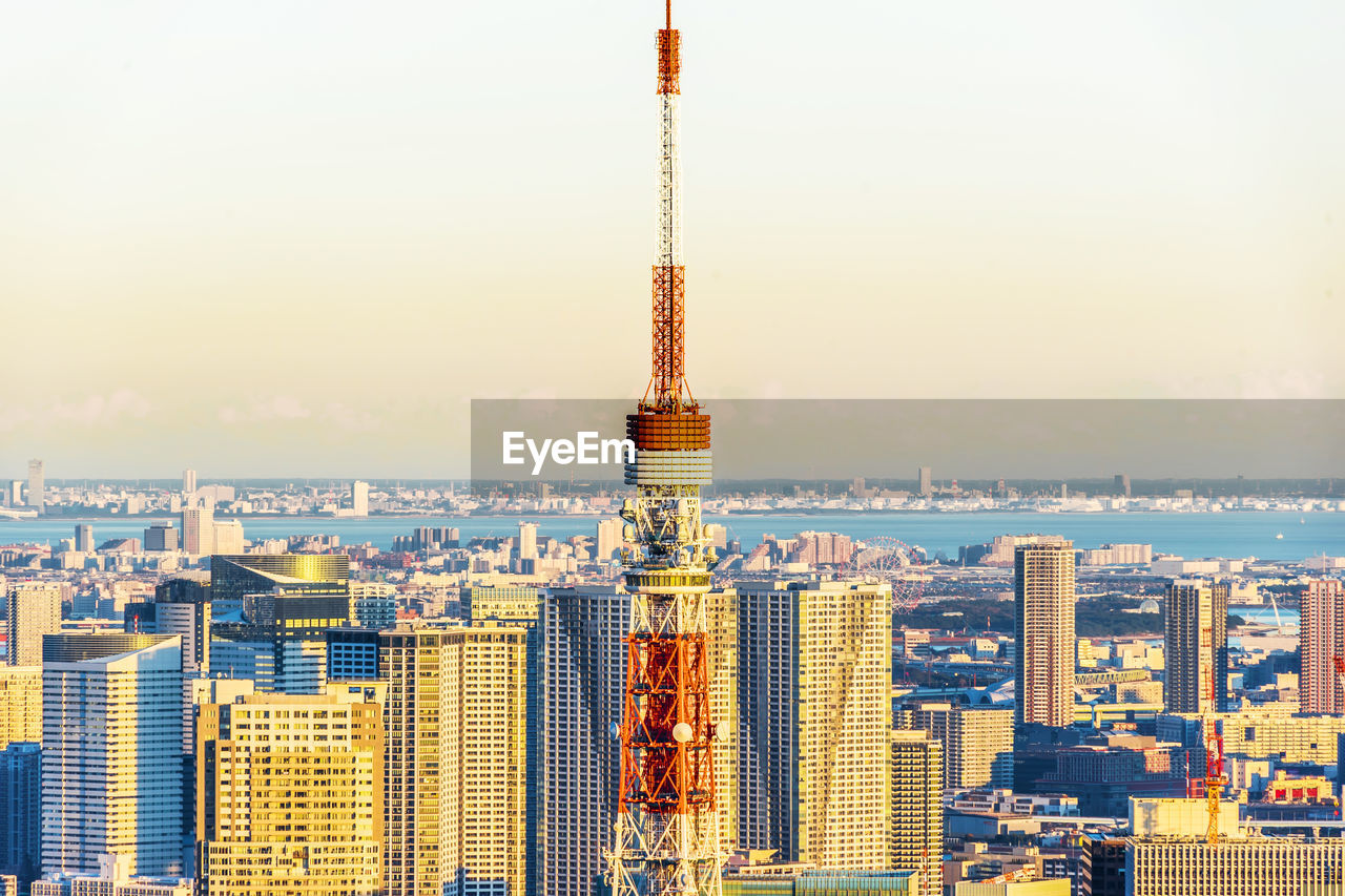 Communications tower amidst cityscape against clear sky