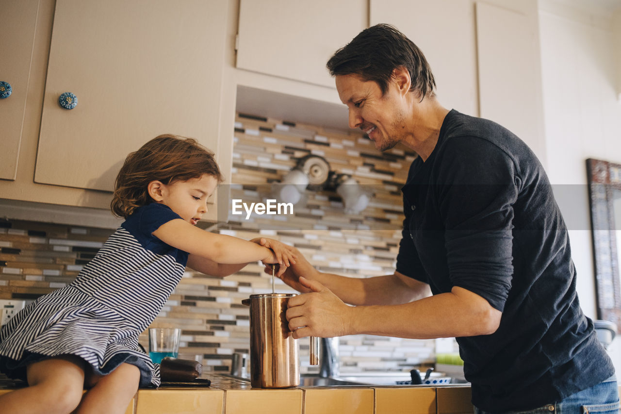 Mature father and daughter working with french press coffee maker in kitchen