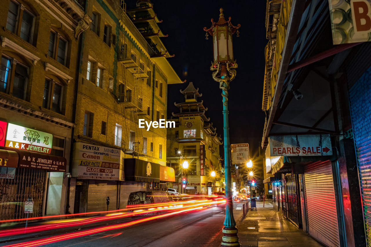 LIGHT TRAILS ON STREET AMIDST BUILDINGS AT NIGHT