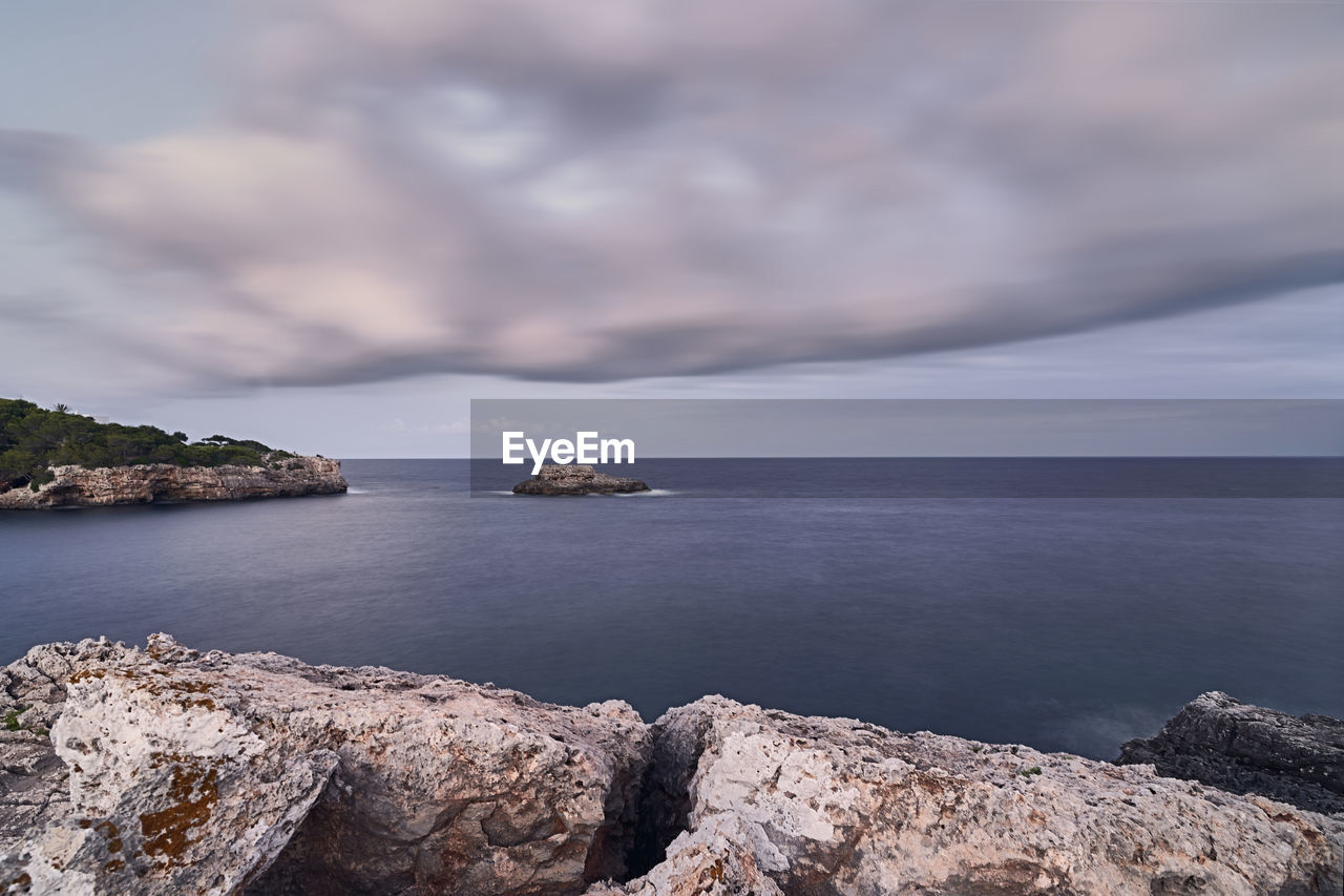 ROCKS BY SEA AGAINST SKY