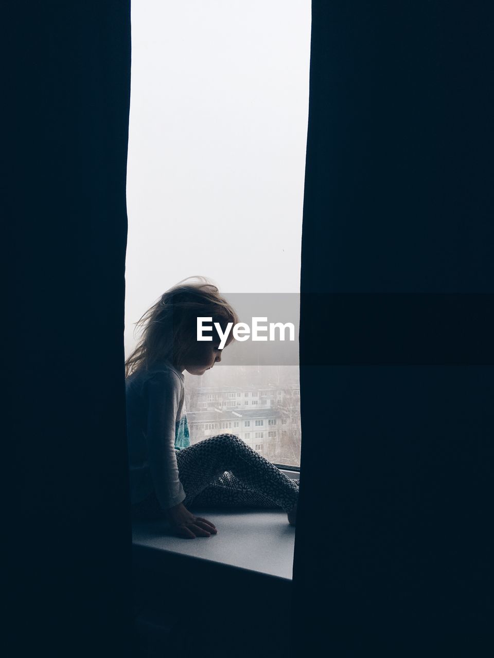 Side view of girl sitting by window at home