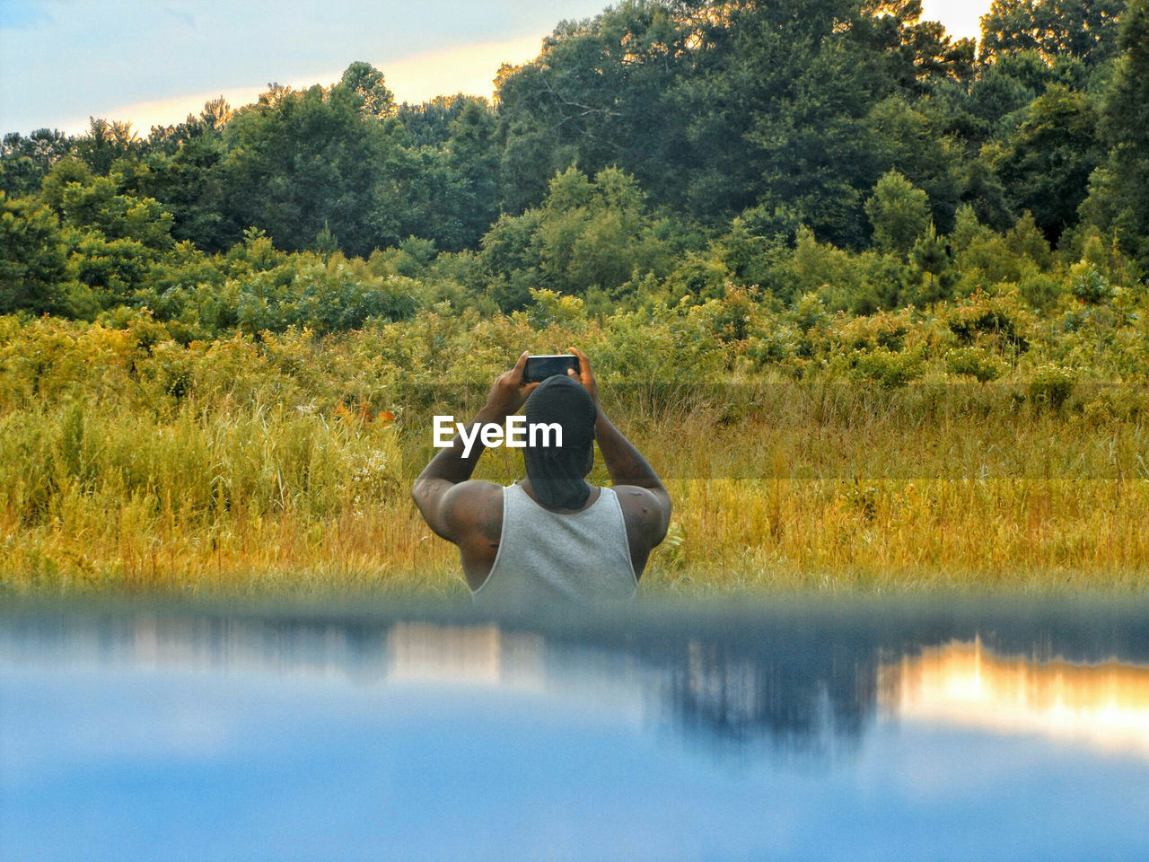 Rear view of man photographing from mobile phone against trees