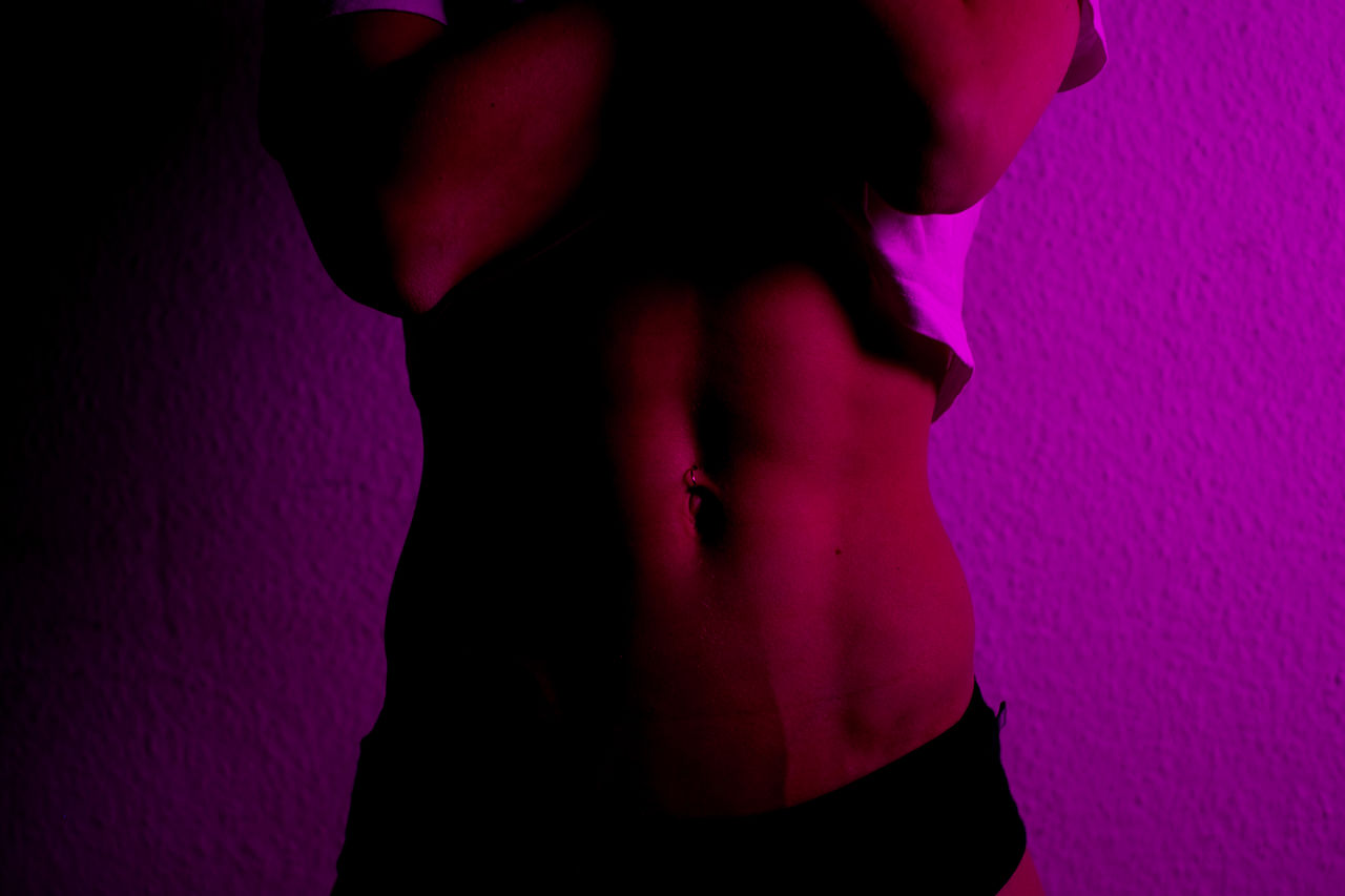 Midsection of woman standing against wall in purple light