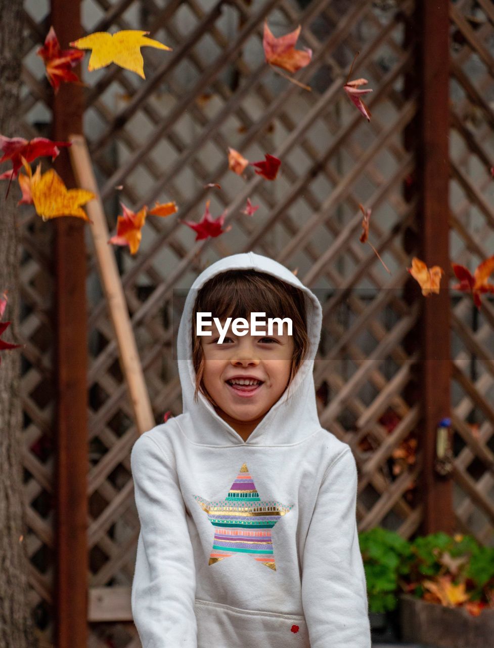 Portrait of cute girl throwing leaves standing outdoors during autumn