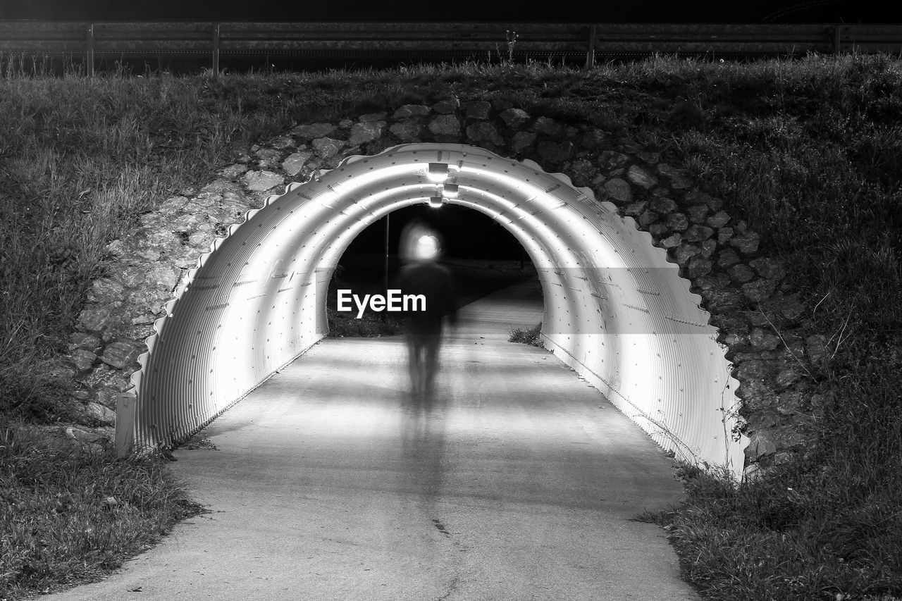 REAR VIEW OF MAN WALKING IN TUNNEL