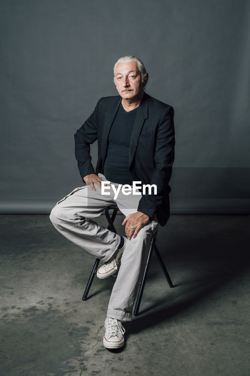 Mature man sitting on chair in front of gray backdrop