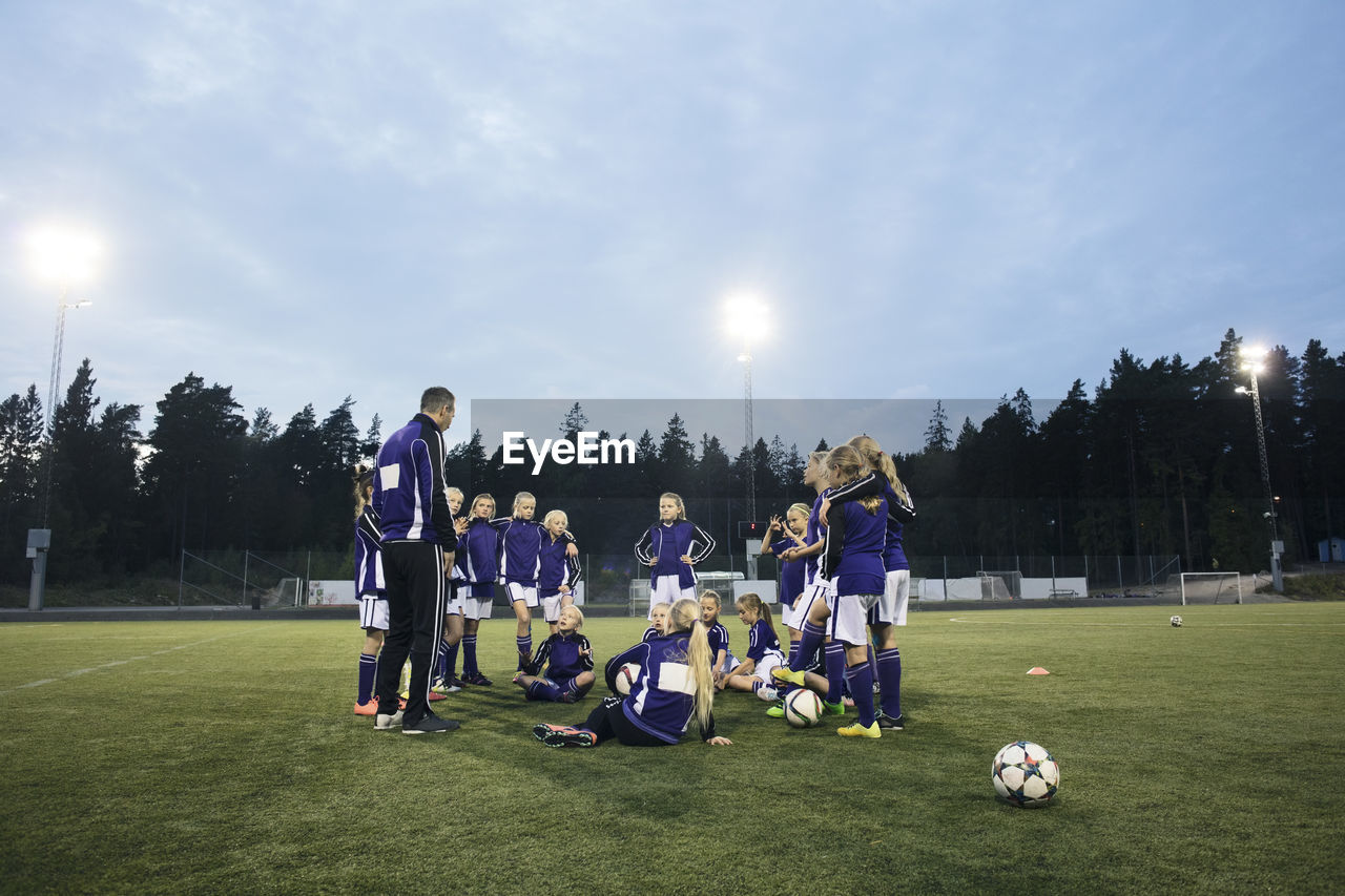 Coach standing by female soccer team on field against sky