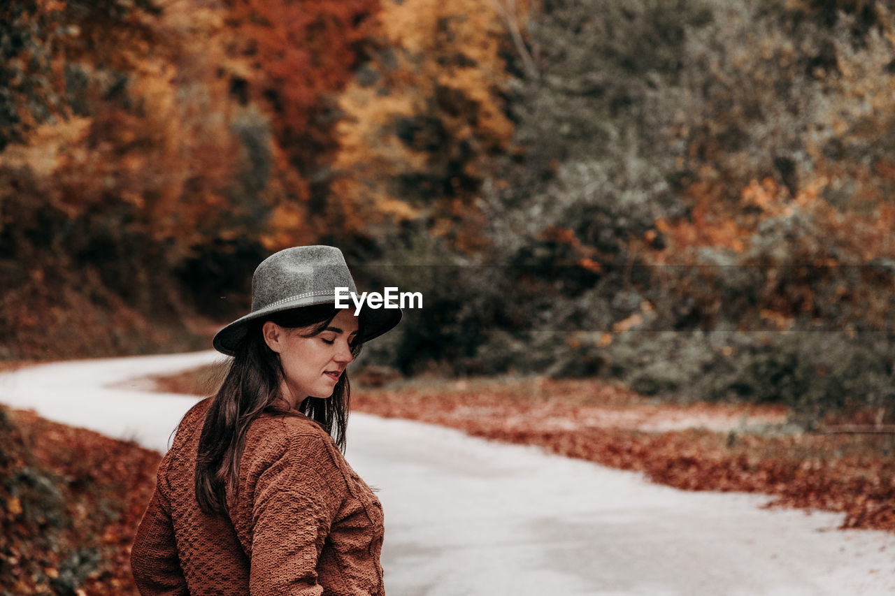 Young woman in autumn clothes on empty road through forest.