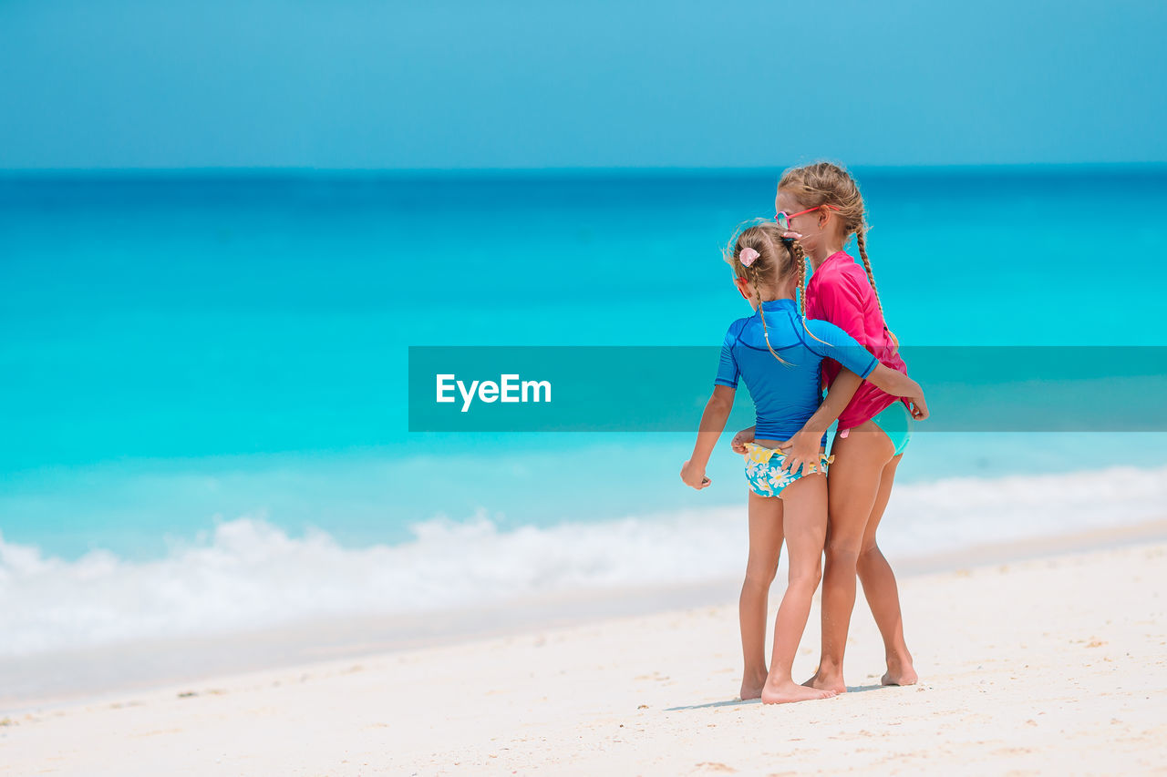 Full length of sisters standing on beach against sea and sky