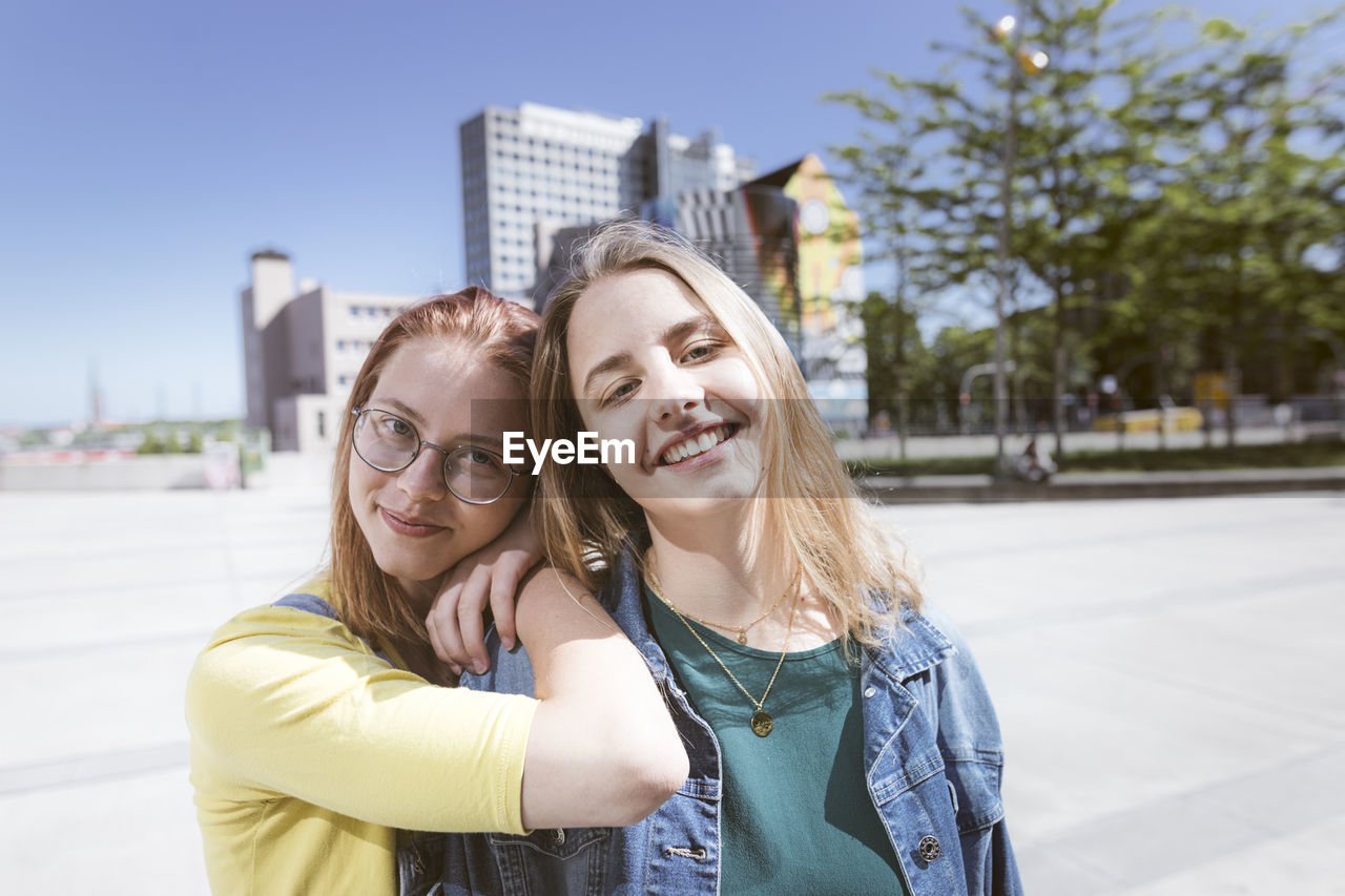 Smiling woman with hands on friend's shoulder in city