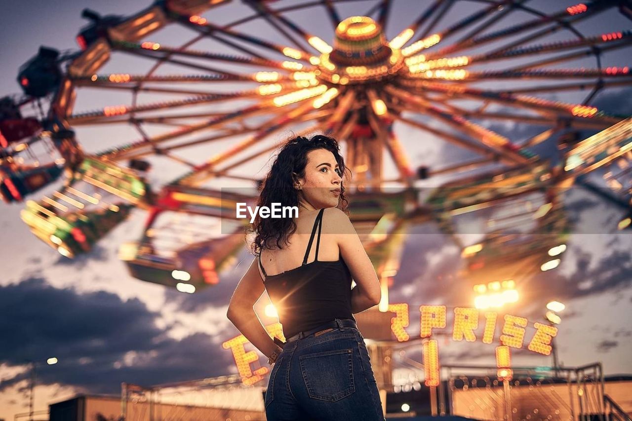 PORTRAIT OF YOUNG WOMAN WITH ILLUMINATED CAROUSEL