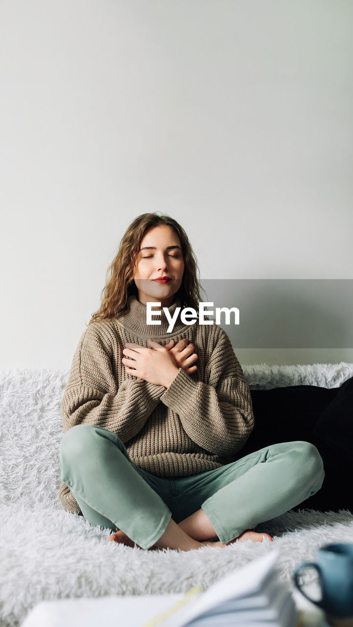 Beautiful young woman in lotus pose on bed practicing pranayama breathing techniques, finding inner