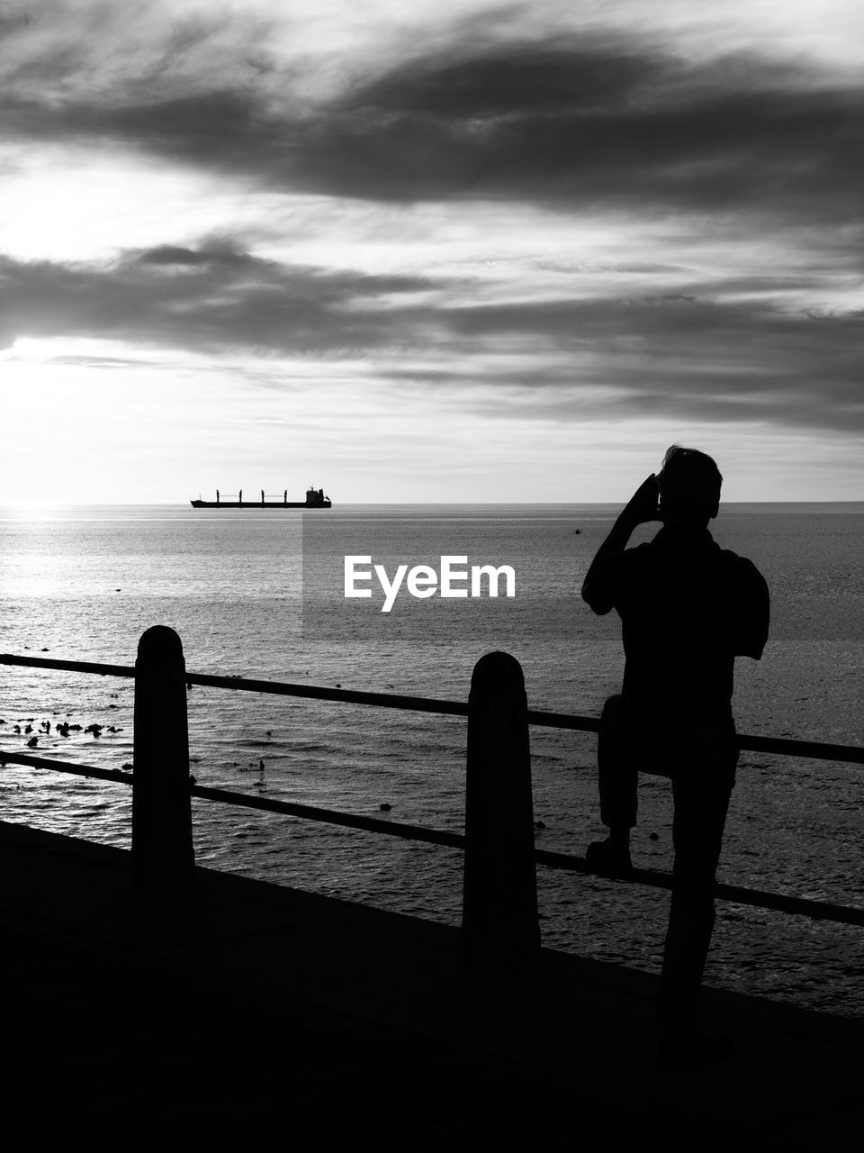 Silhouette man photographing by sea against sky during sunset