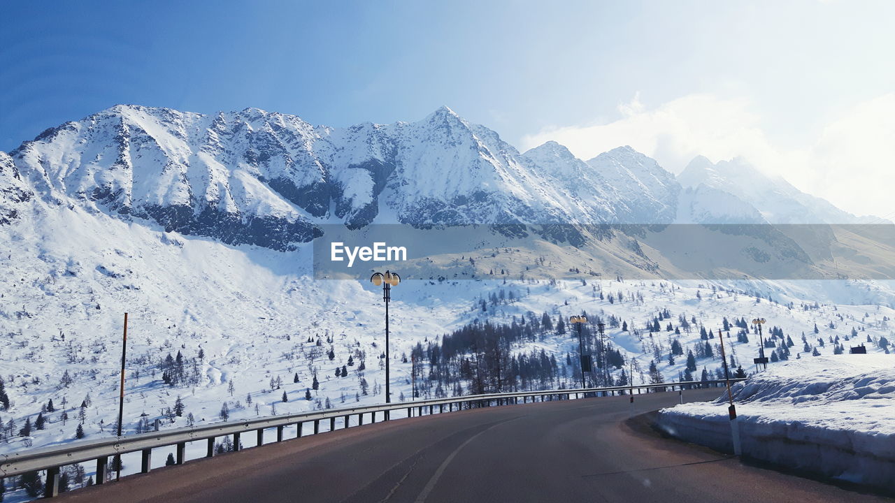 Empty road by snow covered mountains against sky