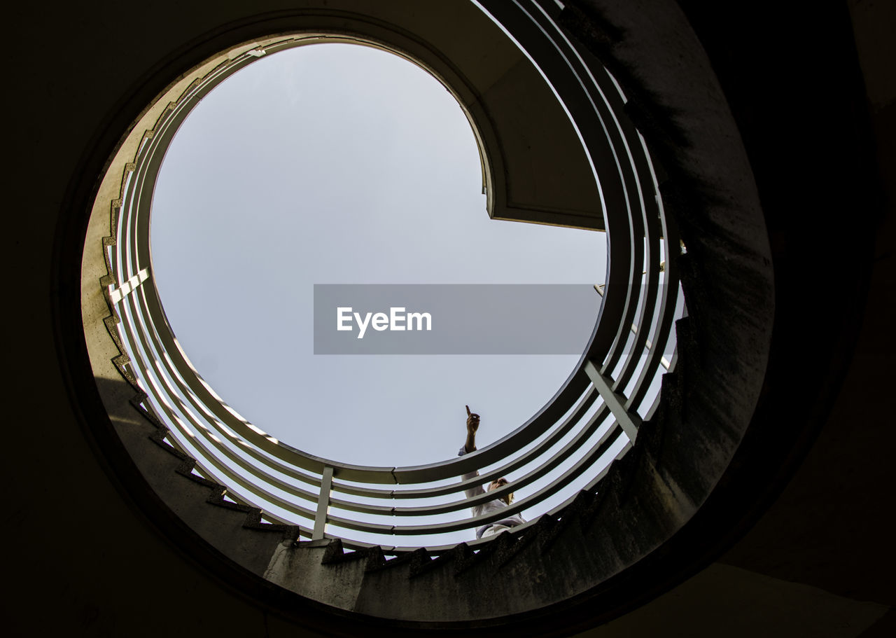 Low angle view of man standing spiral staircase against sky