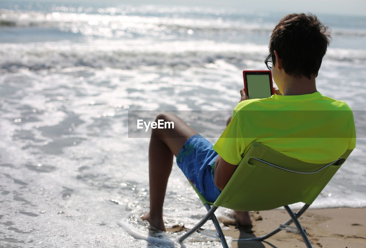 Young teenager reads a digital book on a folding chair by the sea