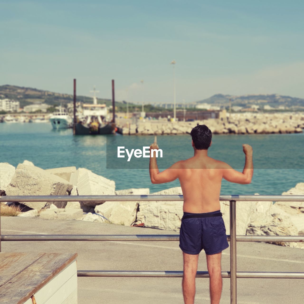 Rear view of shirtless man standing by railing 