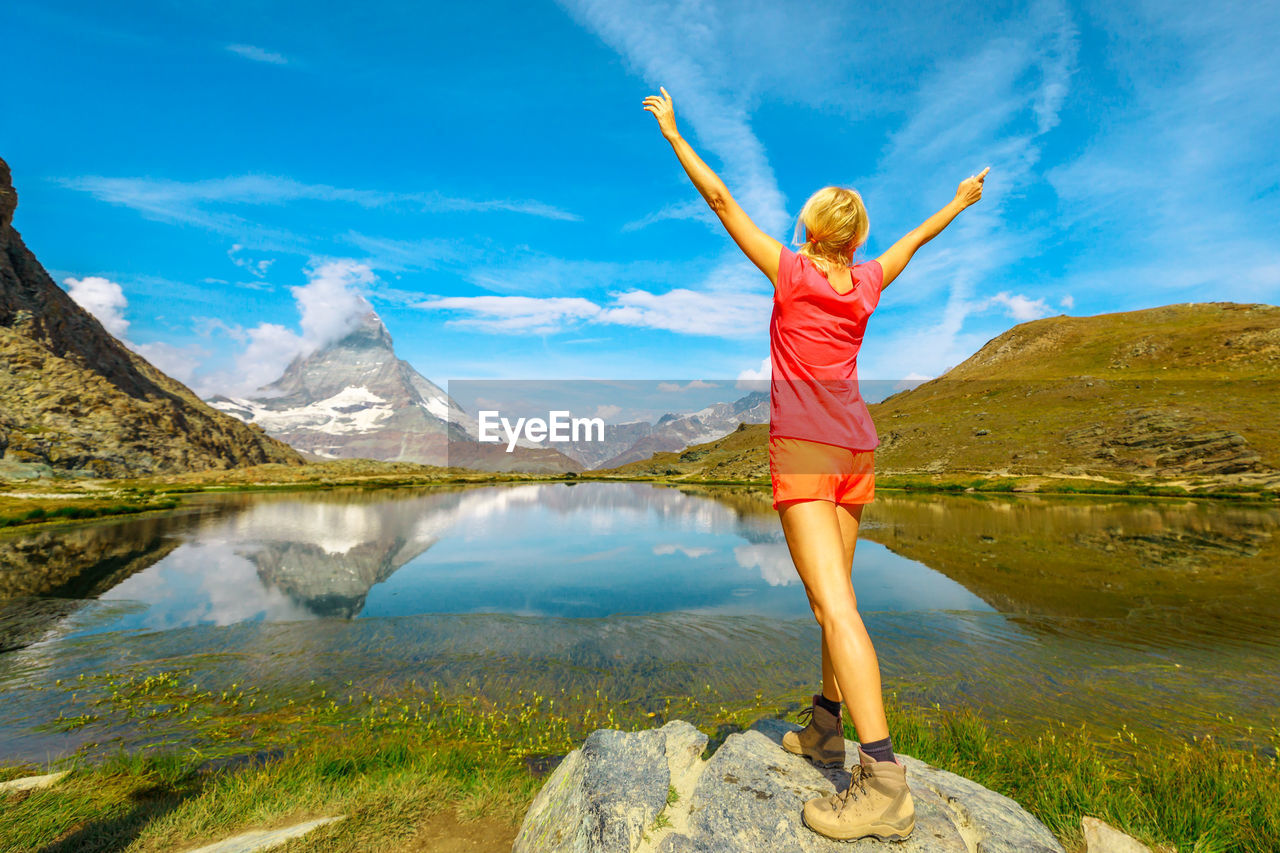 FULL LENGTH OF MAN STANDING BY LAKE AGAINST MOUNTAINS