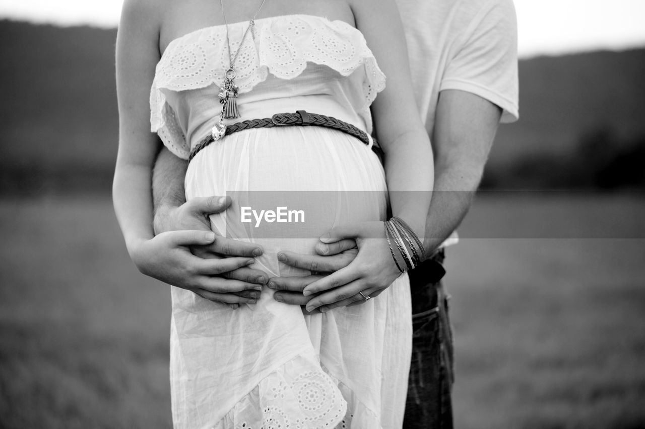 Midsection of couple embracing while standing on field