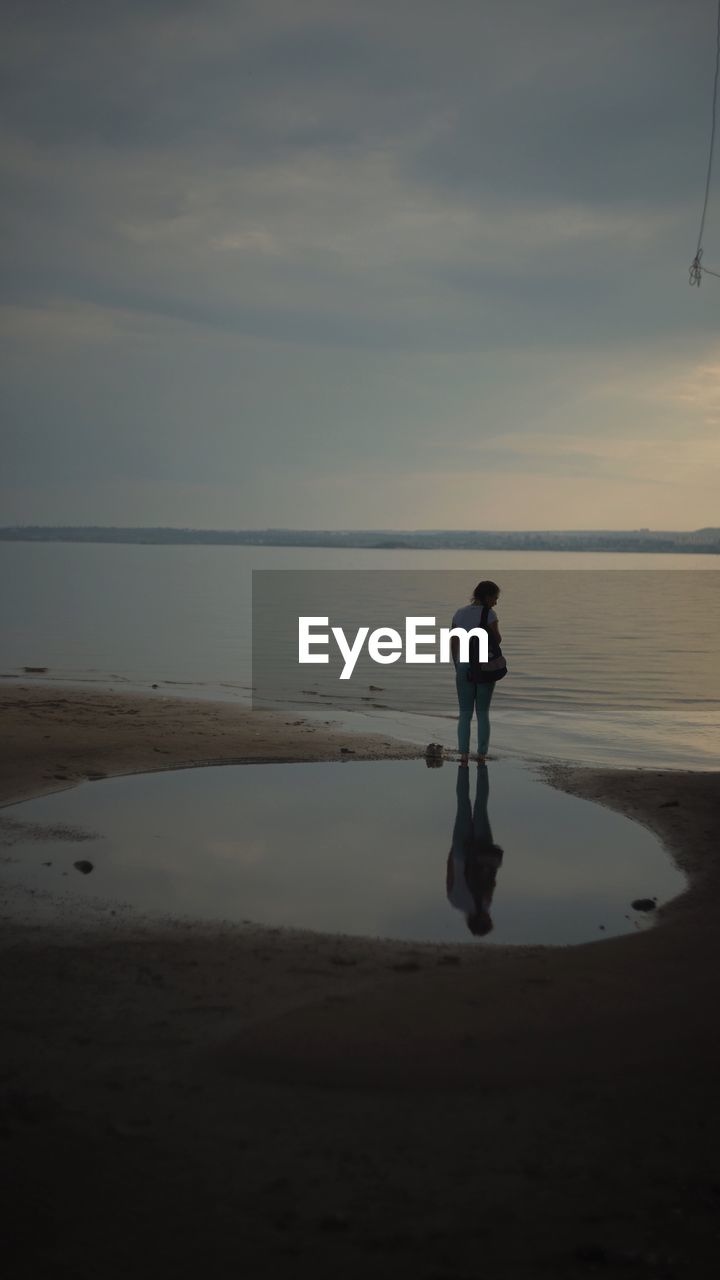 FULL LENGTH OF WOMAN STANDING ON BEACH AGAINST SKY