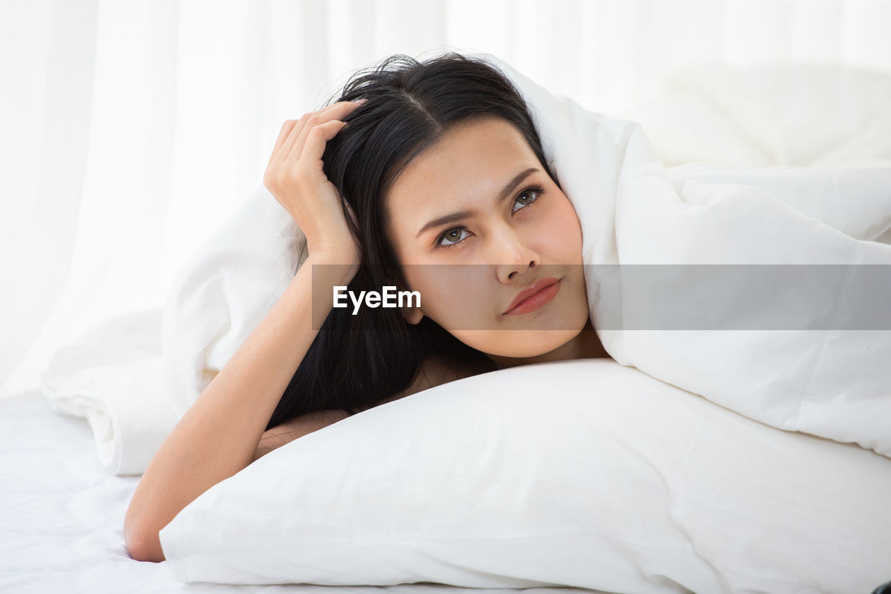 Thoughtful young woman relaxing on bed at home