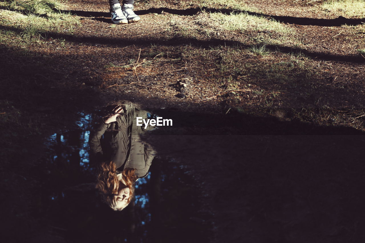 Reflection of woman in water at forest