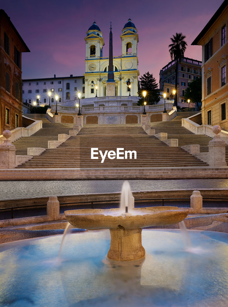 View of fountain by steps heading to built structure against sky at night