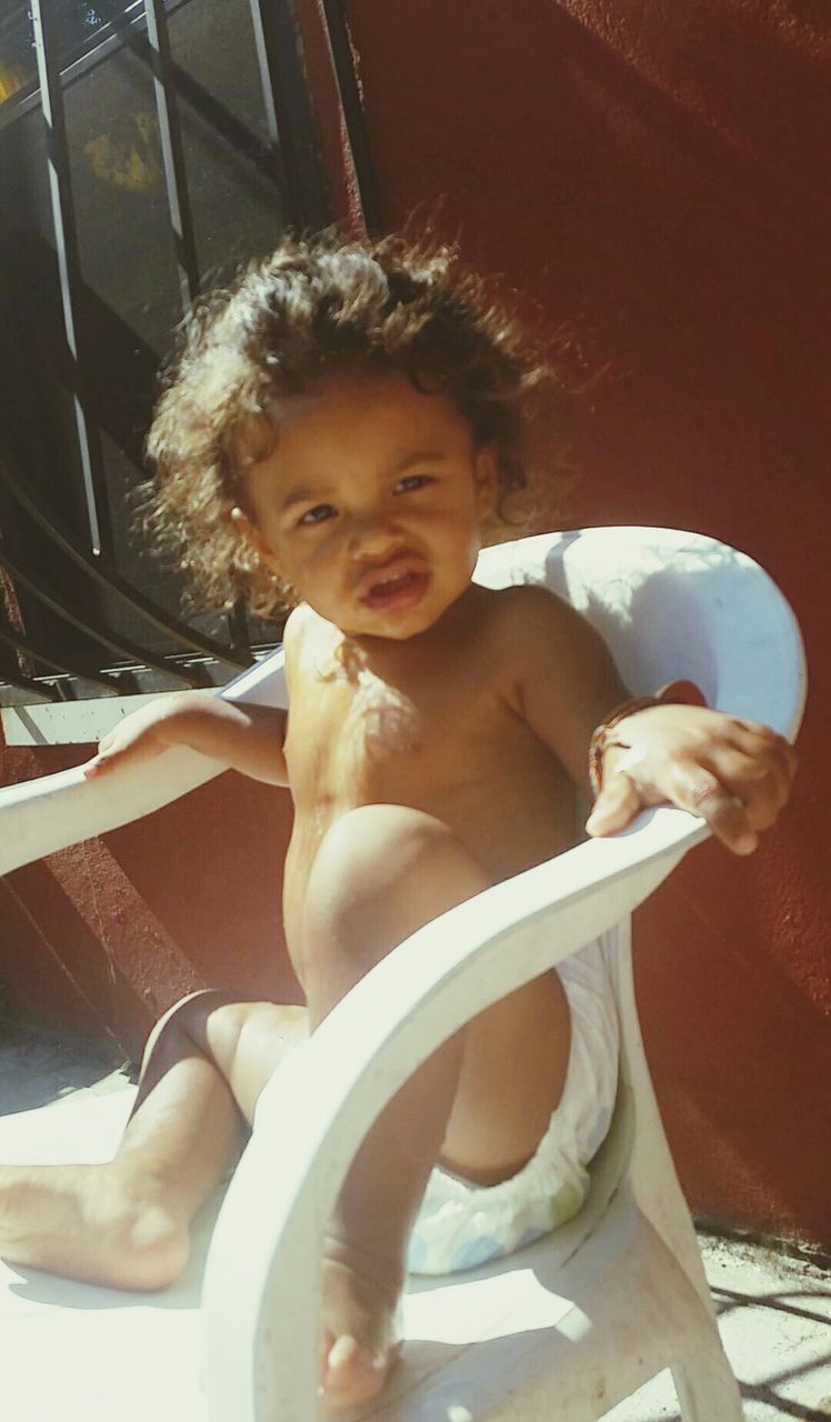 Full length of cute baby boy sitting on chair against wall at home during sunny day