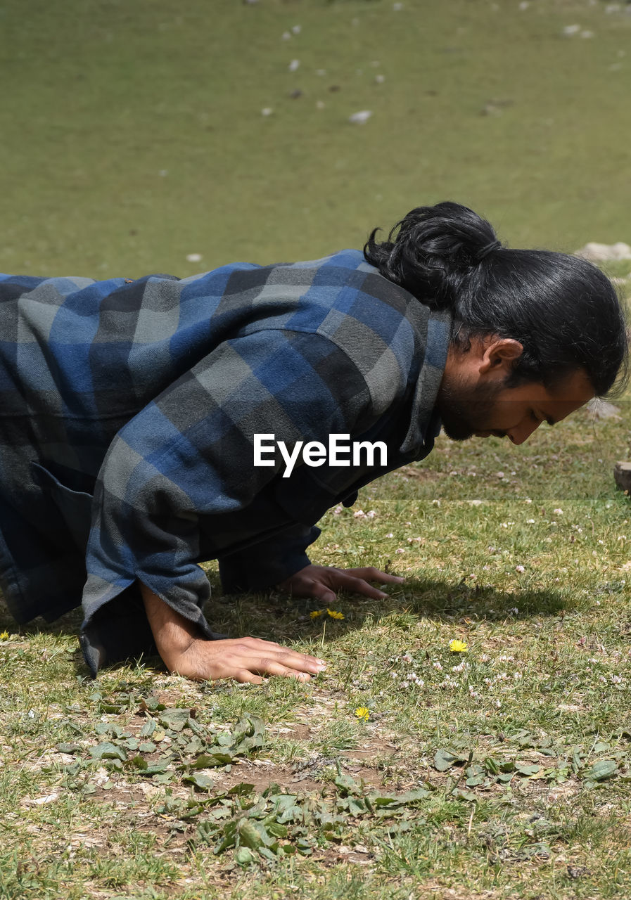Close up side view of a handsome long haired indian young man doing push ups in the mountain