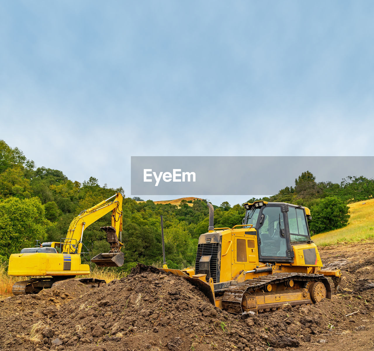 View of yellow bulldozer and excavator on plot of land. heavy equipment clears area. 