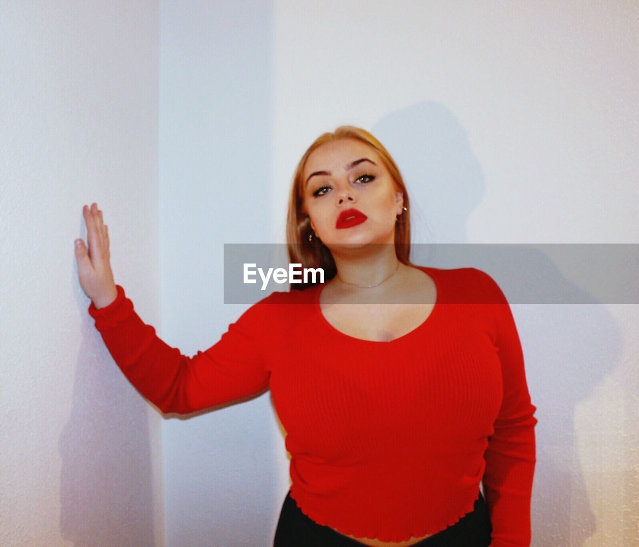 Portrait of young woman wearing red top standing against wall