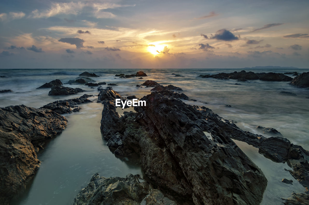 High angle view of rock formations in sea against cloudy sky at sunset
